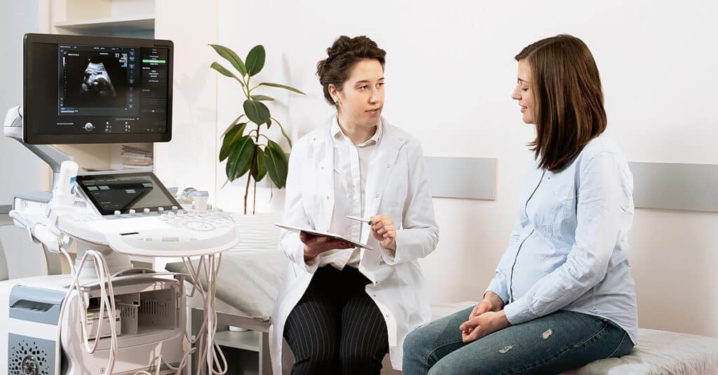 Digital health: A female doctor reviews a pregnant patient’s medical history on a mobile device, showcasing electronic health records and clinical data during the consultation.