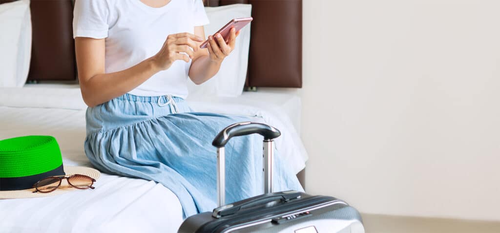 Woman sit on a bed of a hotel room using a mobile device with hospitality solutions for guests