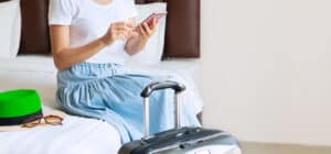 Woman sit on a bed of a hotel room using a mobile device with hospitality solutions for guests