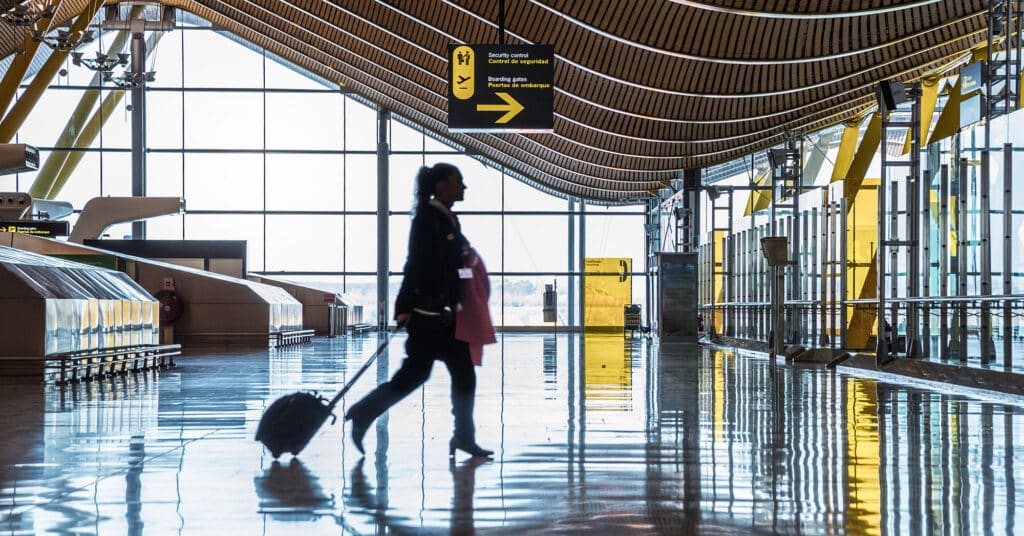 Silhouette of a woman walking with a suitcase through an airport terminal, illustrating modern airport solutions.