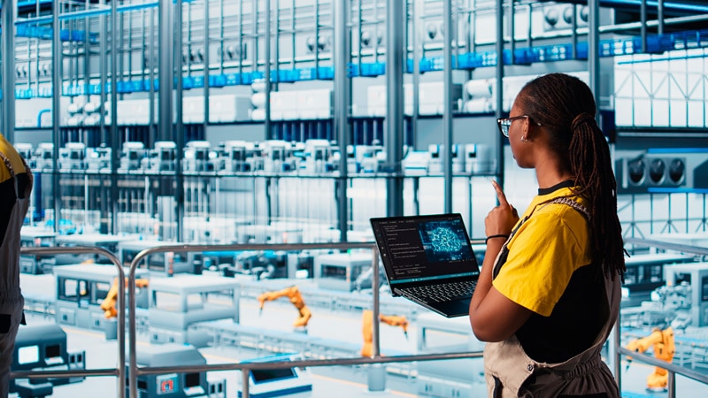 Factory employee checking product manufacturing data on a computer, illustrating IT/OT convergence in action.