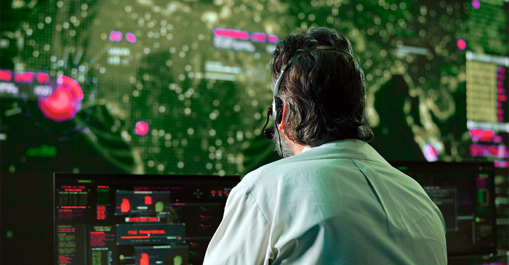 A cybersecurity professional monitors multiple screens in a modern security operations center, analyzing data to detect and prevent IoT security risks.